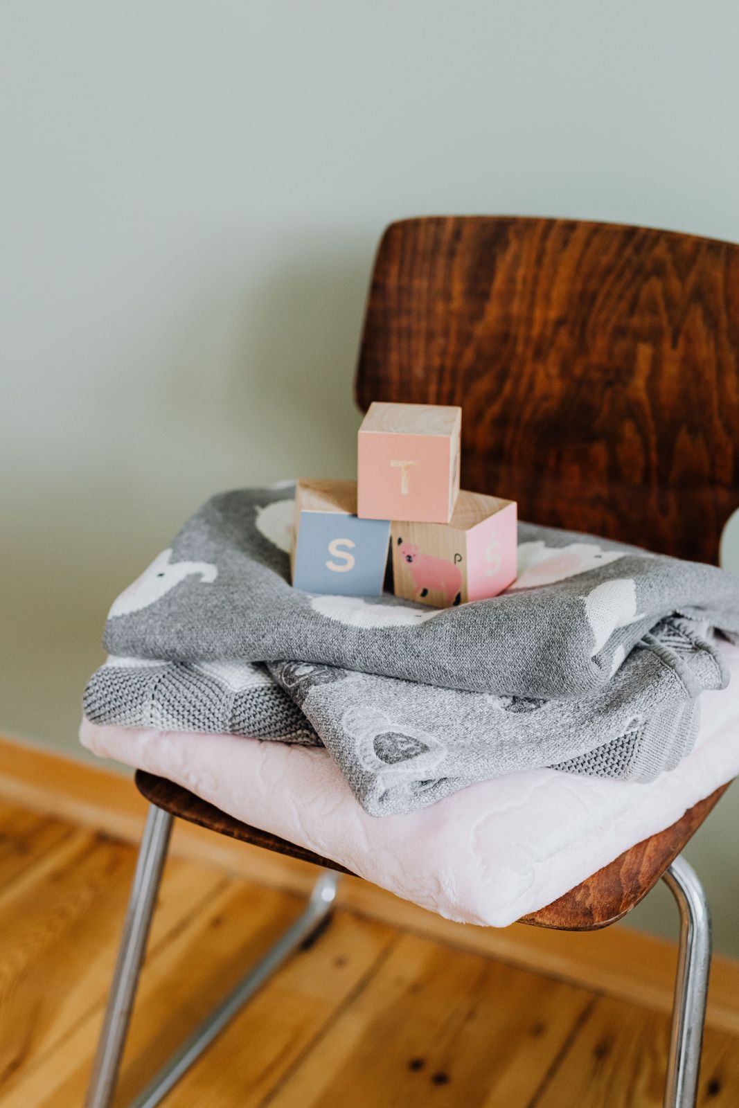 Folded baby blankets and wooden alphabet blocks on a wooden kids chair