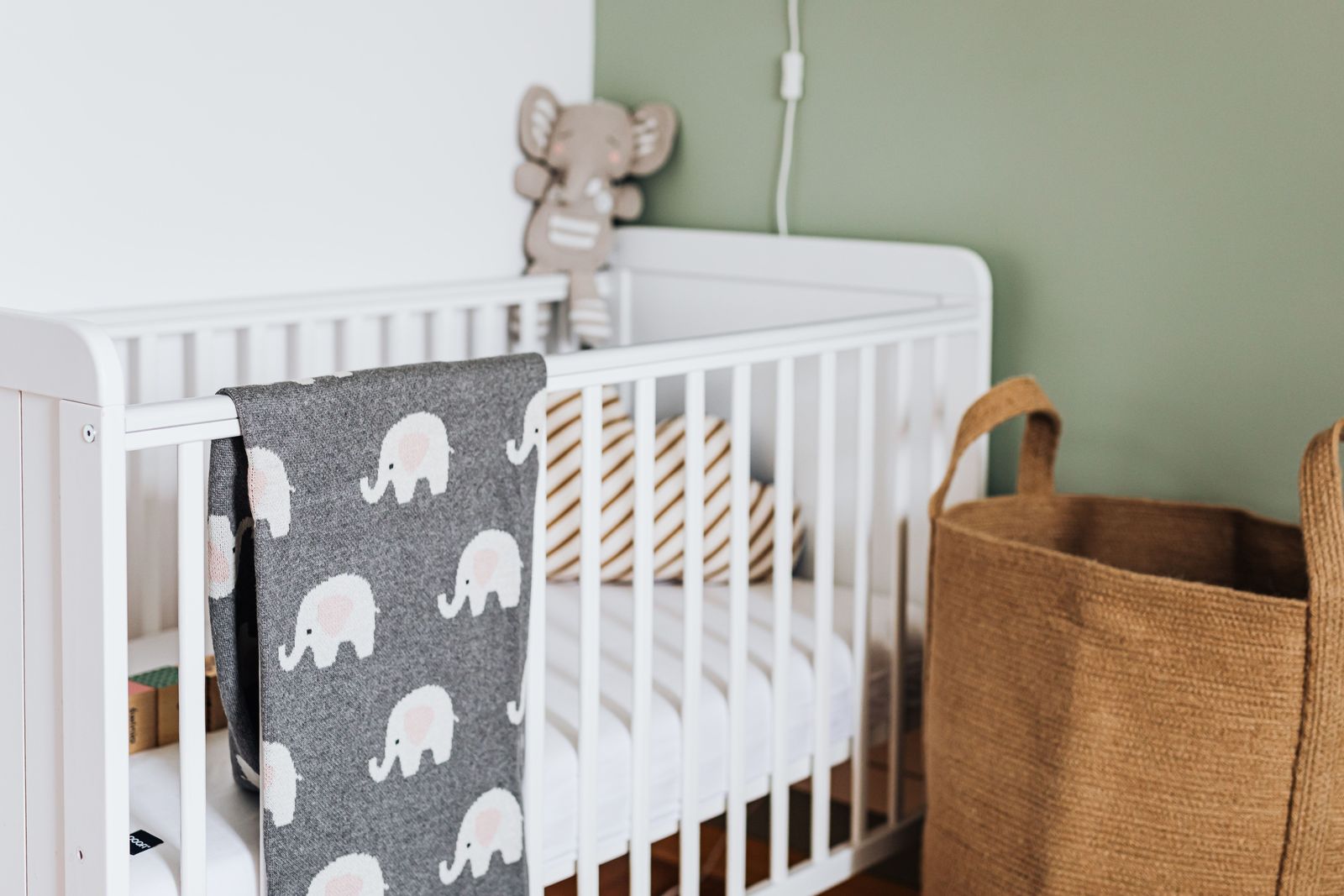 White slatted baby crib with a grey elephant-print blanket over the rail